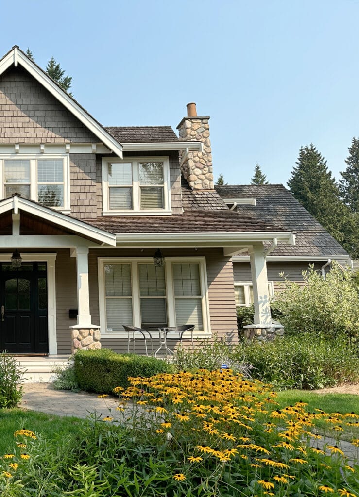 Black front door, greige taupe exterior paint color, warm white trim, beige tan, almond bone windows, cedar shake or shingle roof, river rock fireplace detail