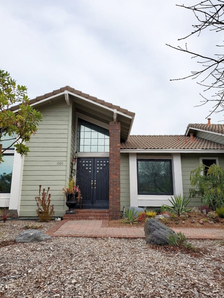 Exterior, terra cotta tile roof, orange pink tones, stone and brick, green painted siding, light greige trim, Wrought Iron painted front door