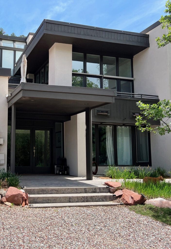 Exterior with orange pink rock and stone, Sherwin Williams taupe paint color, Black Fox trim and black windows