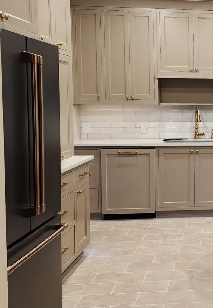 GE Cafe Matte Black appliances, brushed bronze hardware, beige tile floor, Sherwin Williams mushroom greige taupe painted kitchen wood cabinets, Cambria Ridgegate off-white quartz, gold hardware