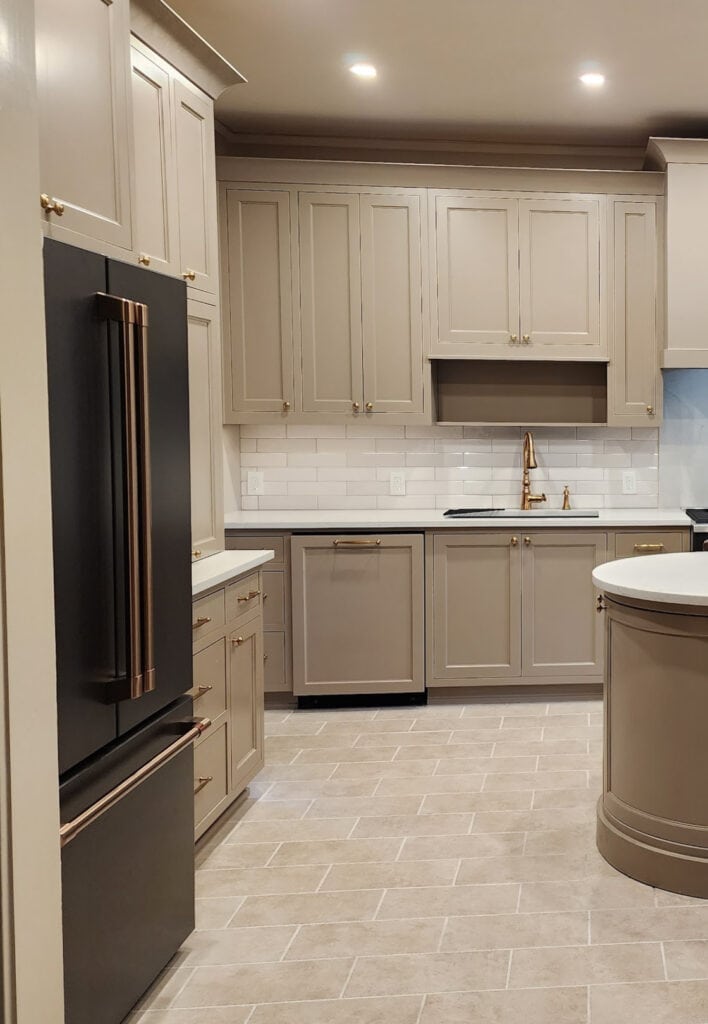 GE Cafe Matte Black fridge, brushed bronze hardware, beige tile floor, Sherwin Williams mushroom greige taupe painted kitchen wood cabinets, Cambria Ridgegate off-white quartz, Stone Hearth walls