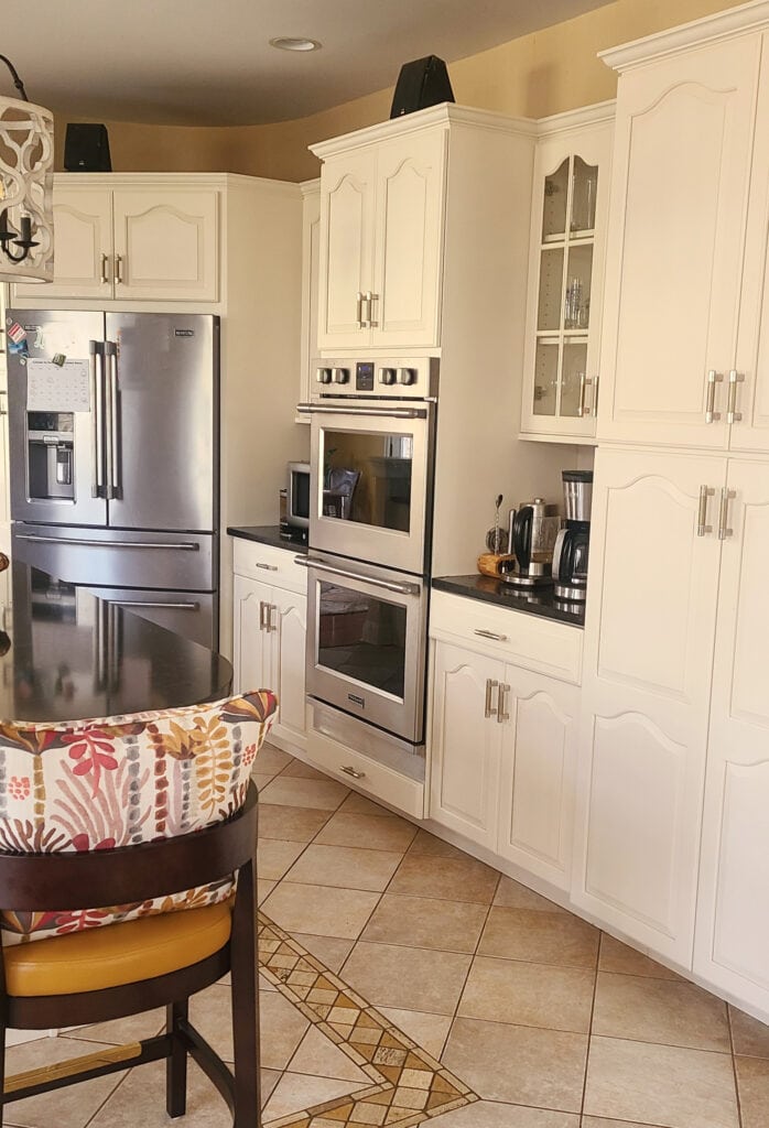 Kitchen with black granite countertop, beige travertine tile floor, painted cathedral wood cabinets, Benjamin Moore Maritime White, off-white beige