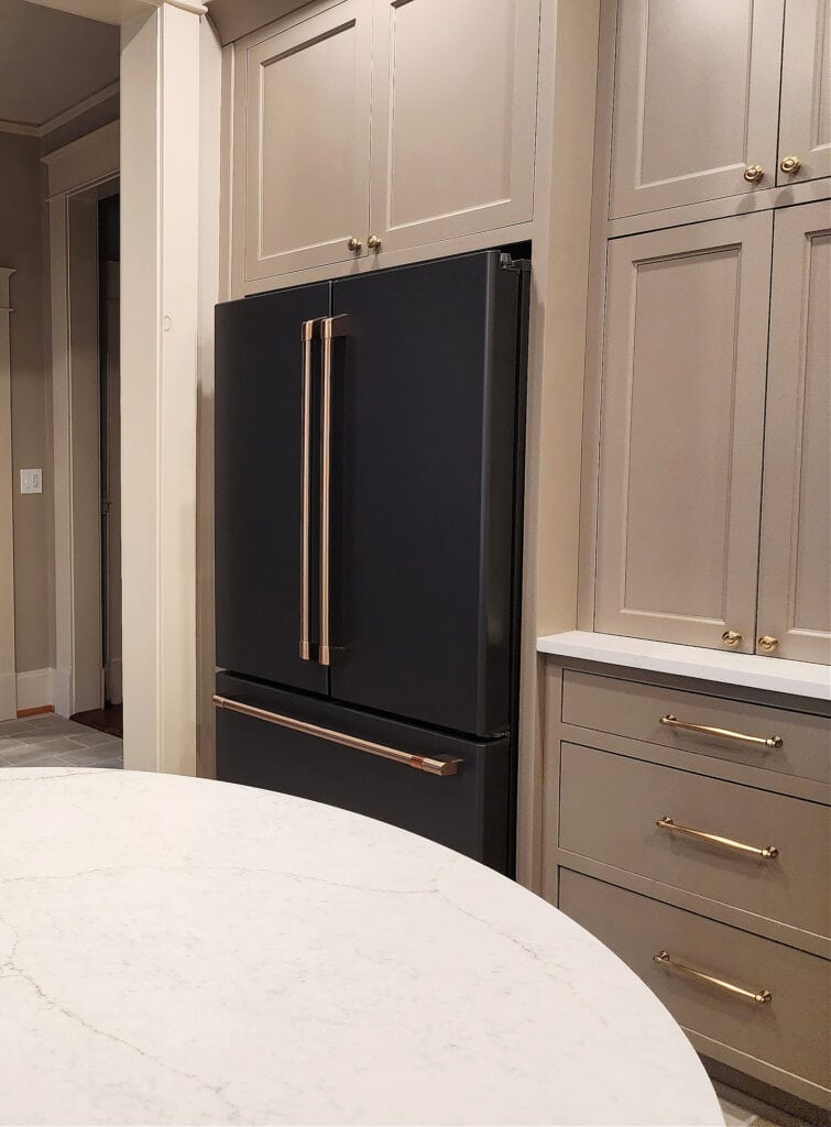 Kitchen with painted cabinets in mushroom, dark beige greige paint color, GE Cafe Matte black Fridge with brushed bronze of brass hardware finish, hardware