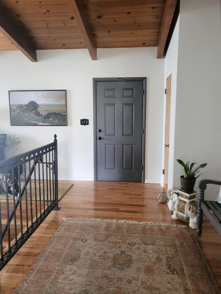 Sherwin Williams Heron Plume off-white paint color on walls, Benjamin Moore Kendall Charcoal on inside of front door, wood beam, mid century ceiling, tongue and groove, wood floor, black railing