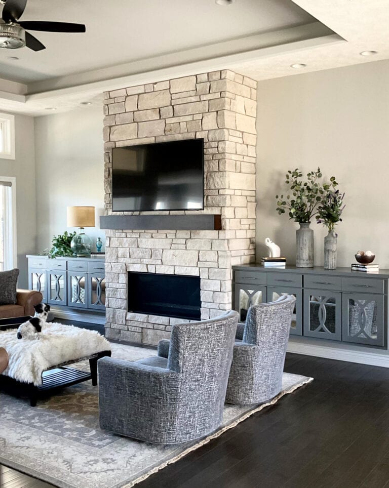 Sherwin Williams Repose Gray in living room, limestone look fireplace with tv above. Brown leather, dark wood floor, high reflective white trim (1)