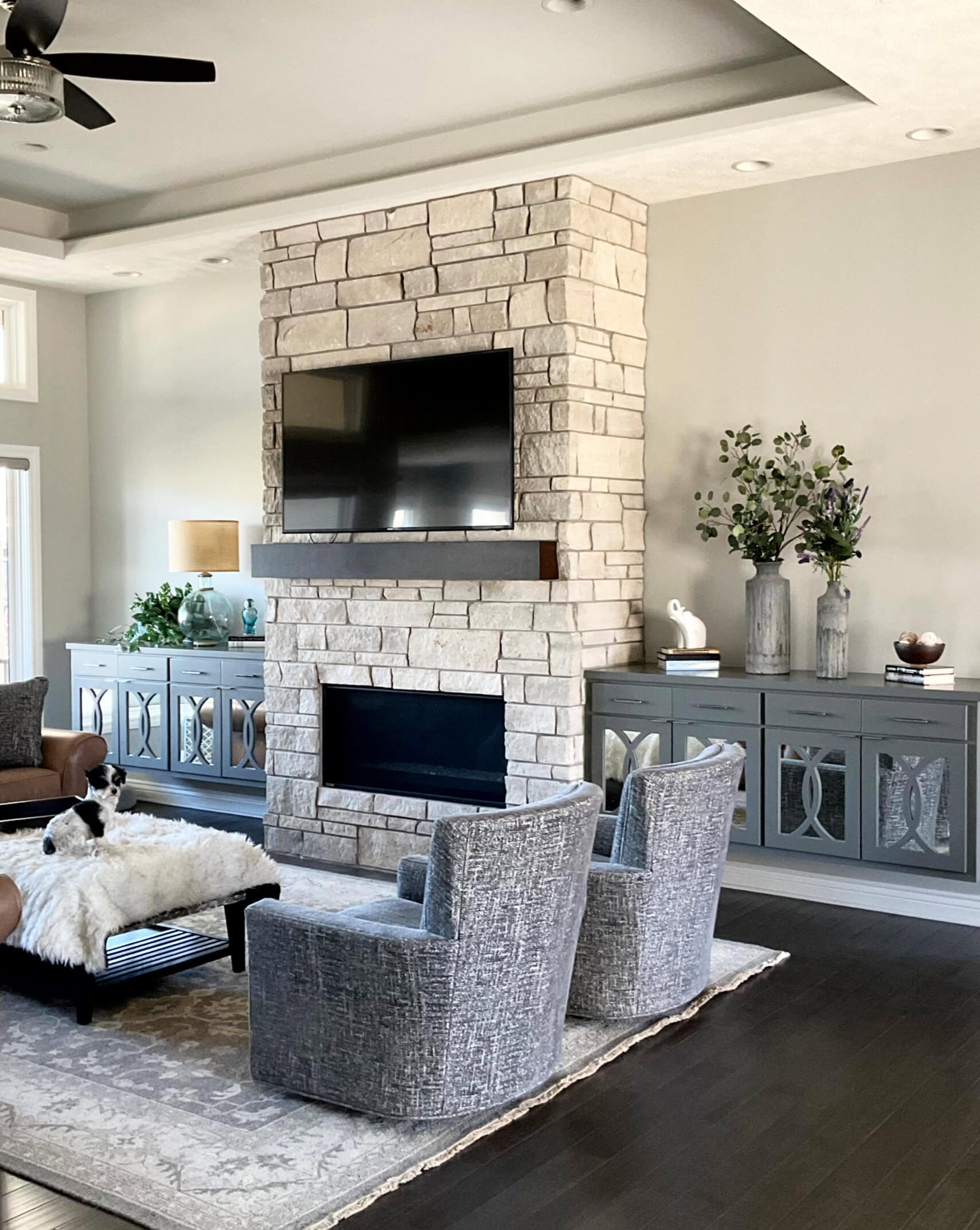 Sherwin Williams Repose Gray in living room, limestone look fireplace with tv above. Brown leather, dark wood floor, high reflective white trim (1)