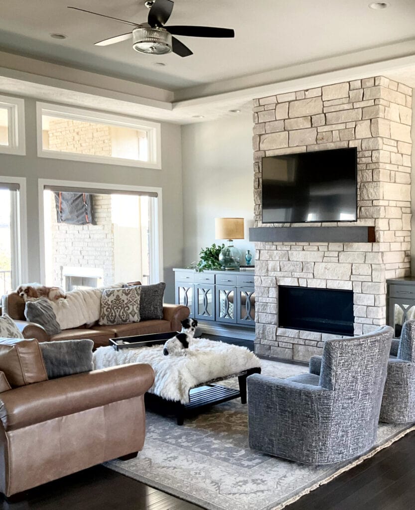 Sherwin Williams Repose Gray in living room, limestone look fireplace with tv above. Brown leather, dark wood floor, high reflective white trim