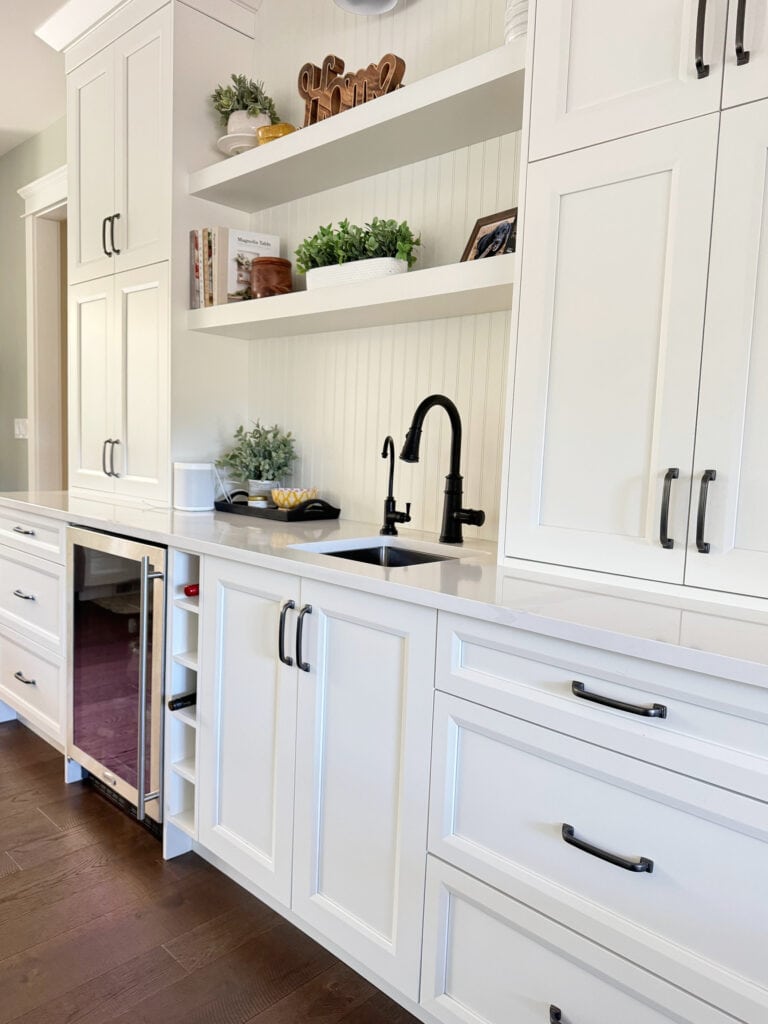Sherwin Williams white painted kitchen cabinets, dark wood floor, black hardware and faucet, bar, beverage station in kitchen, Silestone, Cosentino Et Calacatta Gold white quartz, beadboard backsplash