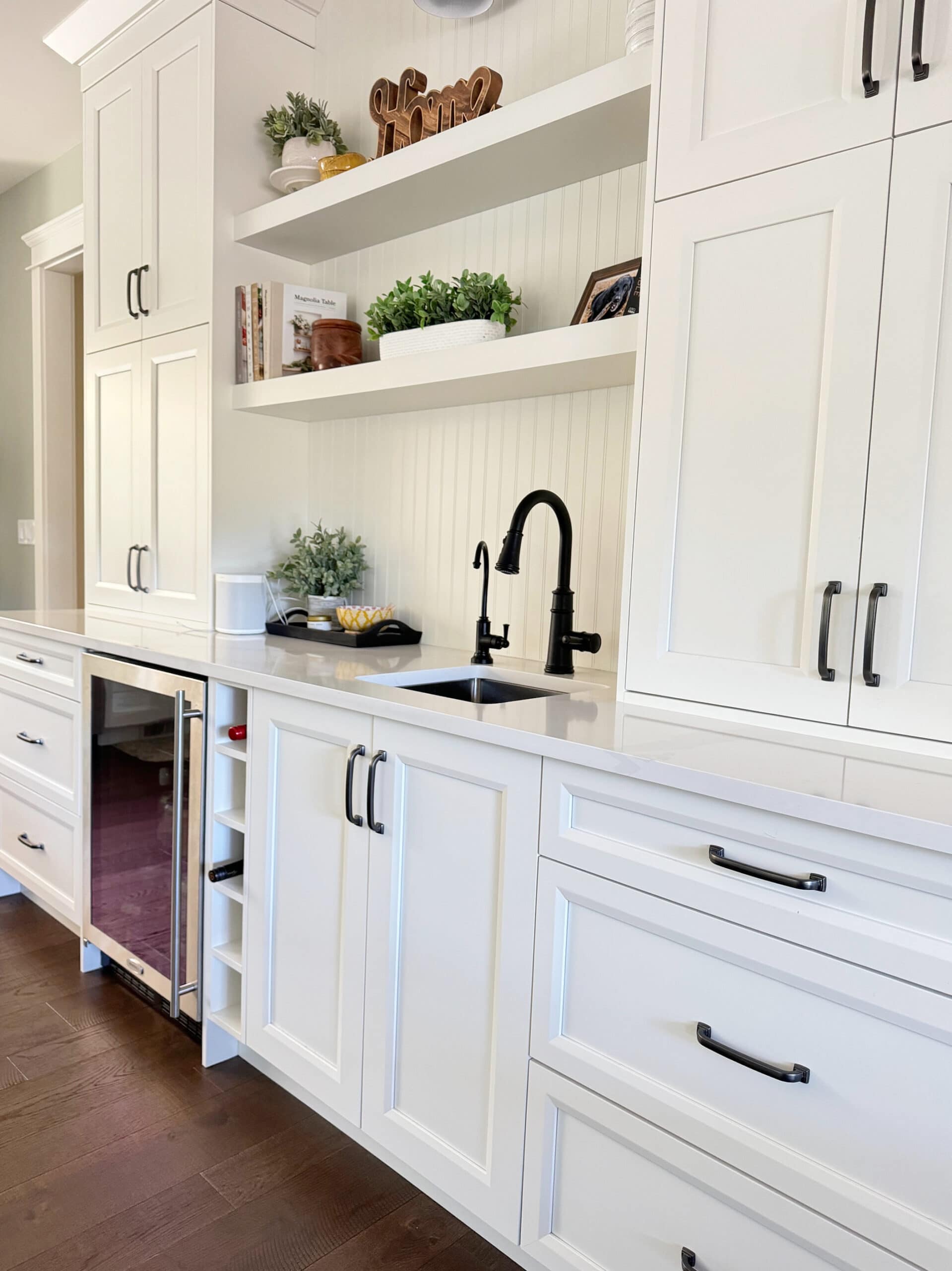 Sherwin Williams white painted kitchen cabinets, dark wood floor, black hardware and faucet, bar, beverage station in kitchen, Silestone, Cosentino Et Calacatta Gold white quartz, beadboard backsplash