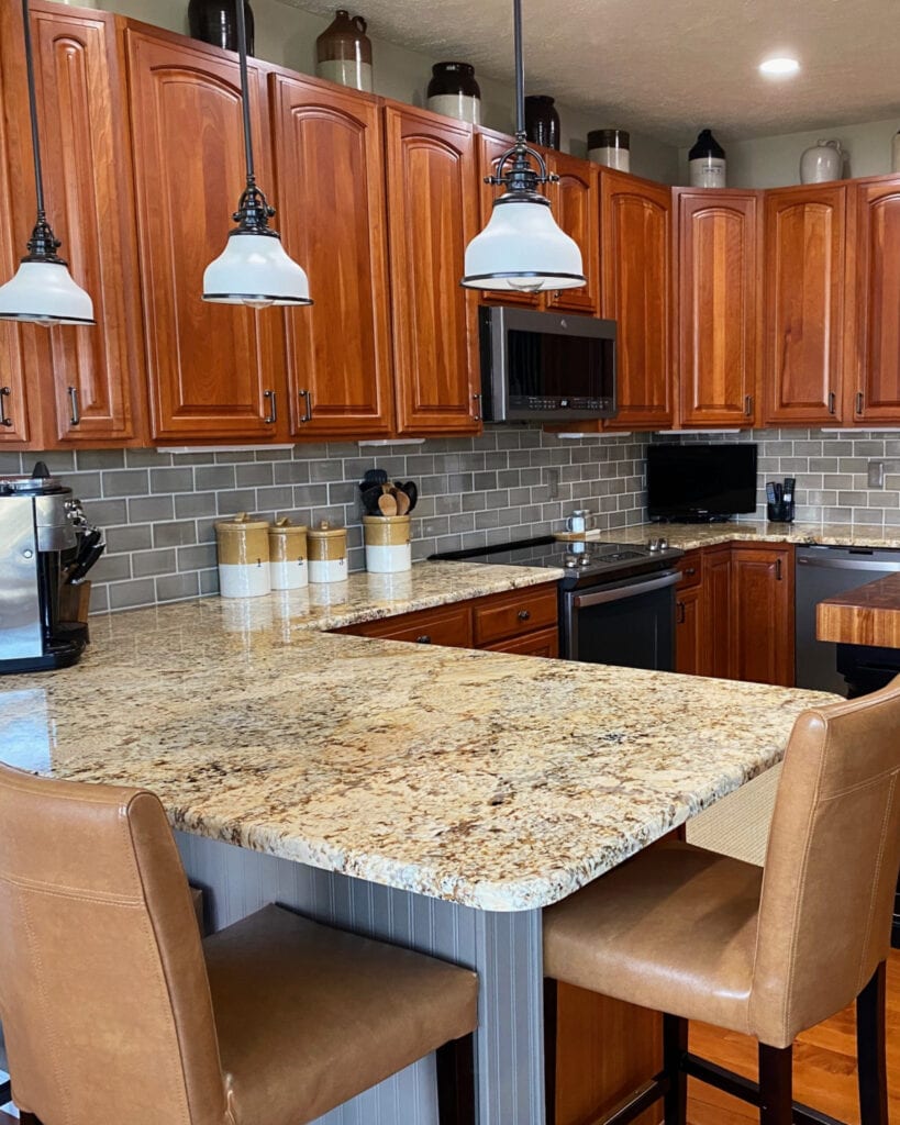 Solarius granite warm granite countertops, cherry orange red stained wood kitchen cabinets, greige taupe subway tile backsplash, Sherwin Tony Taupe painted peninsula cabinet