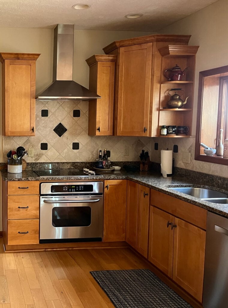 Tuscan style maple or wood kitchen cabinets, travertine tile backsplash black granite countertop, wood floor, CAnvas Tan on walls