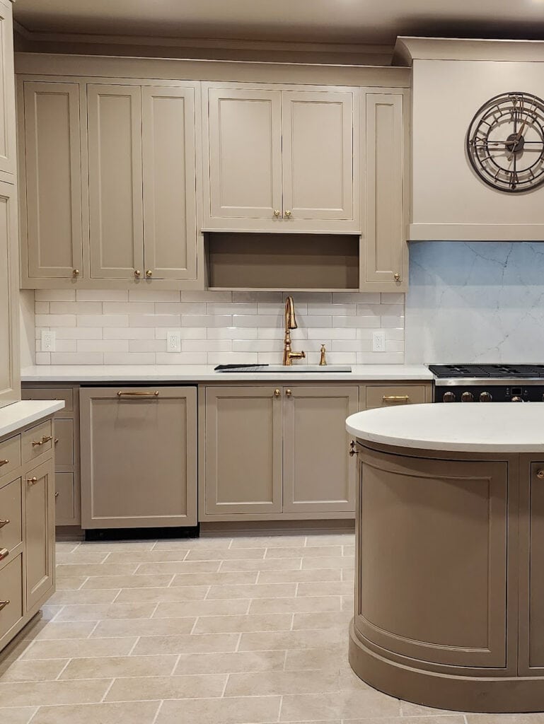 travertine look tile floor, mushroom greige Sherwin Williams painted kitchen cabinets, gold hardware, faucet, subway tile backsplash, MSI CALACATTA VALENTIN off-white quartz countertop