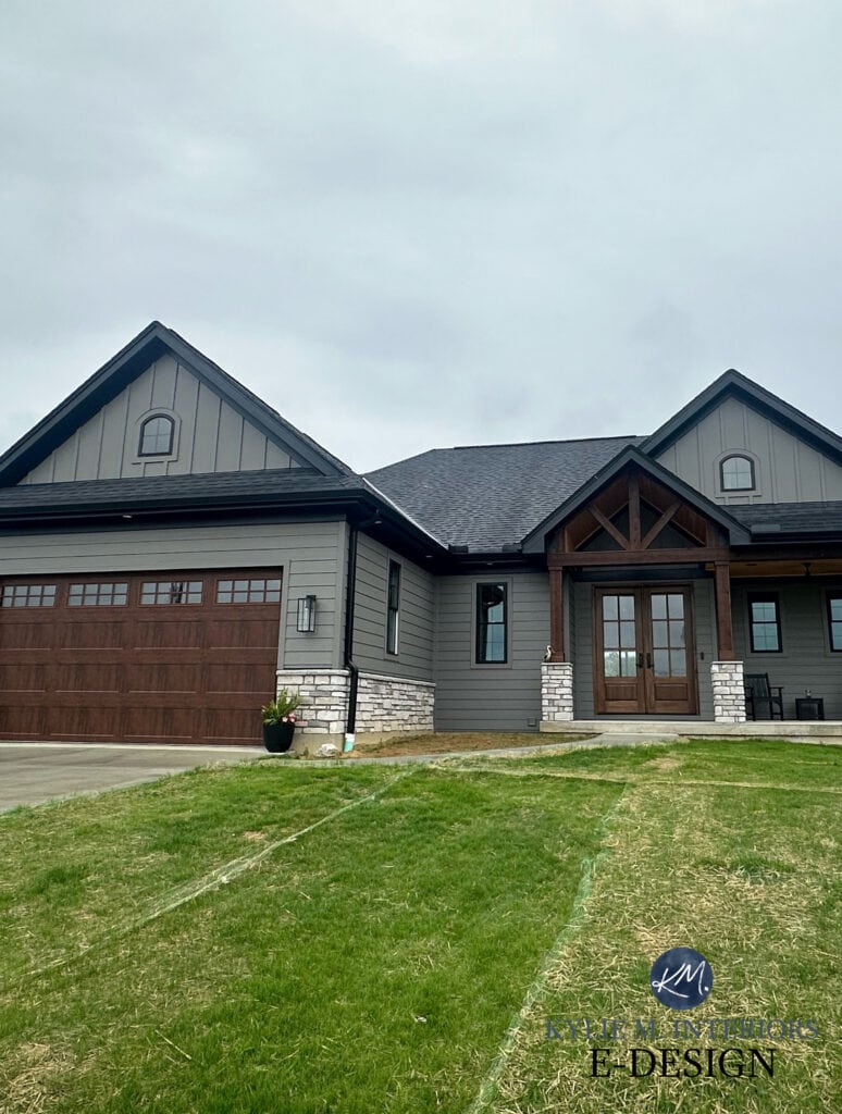 exterior siding painted Sherwin Williams Gauntlet Gray, dark warm gray, fake wood look garage doors, dark wood beams and front door, black asphlat roof, black windows, gutters, exterior stone