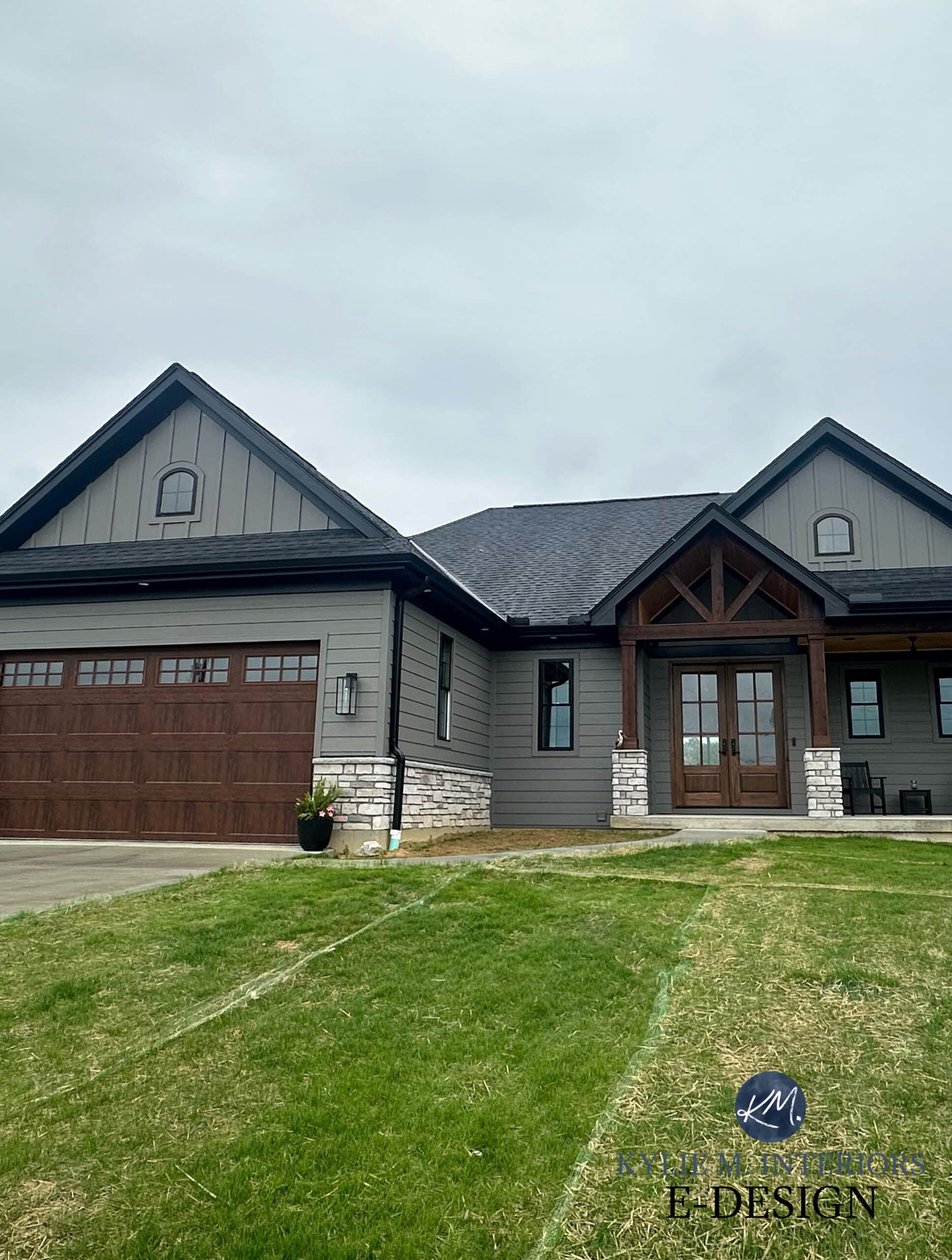 exterior siding painted Sherwin Williams Gauntlet Gray, dark warm gray, fake wood look garage doors, dark wood beams and front door, black asphlat roof, black windows, gutters, exterior stone