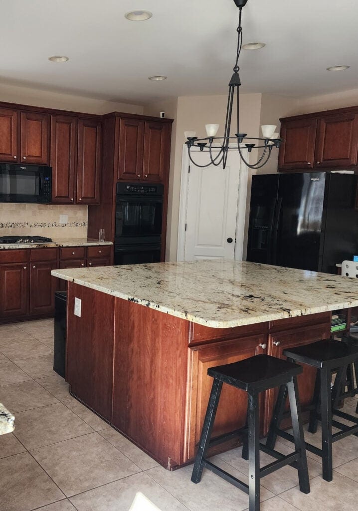 large kitchen with red cherry stained wood cabinets, travertine tile backsplash, beige tile floor, beige, cream, taupe granite countertops, large island, update ideas, black appliances