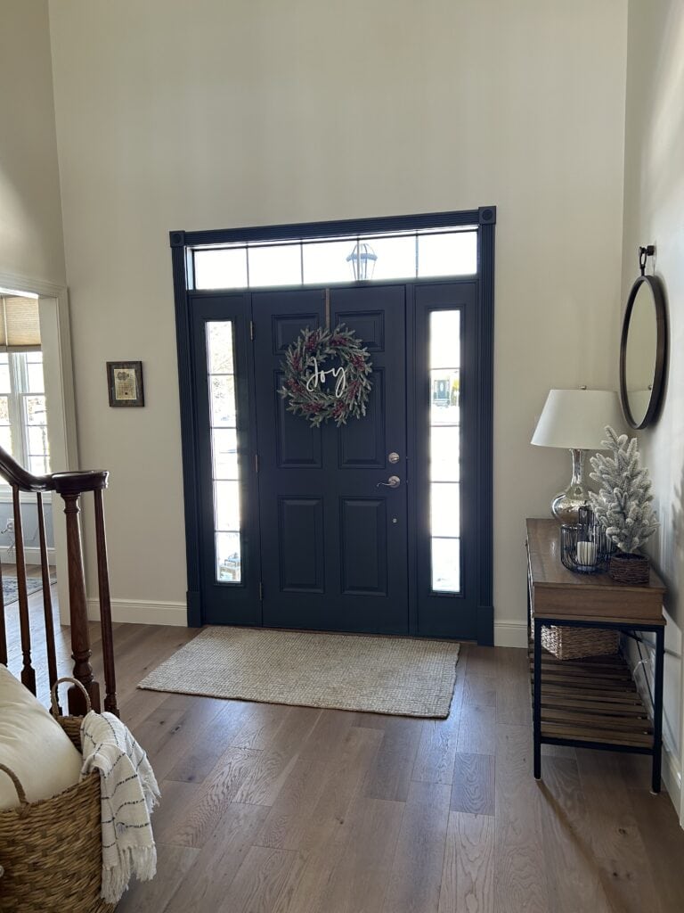 Benjamin Moore Wrought Iron Front door, Pearly White Sherwin Williams off-white paint color on walls, oak wood floor. Oak staircase. Entryway. Kylie M.