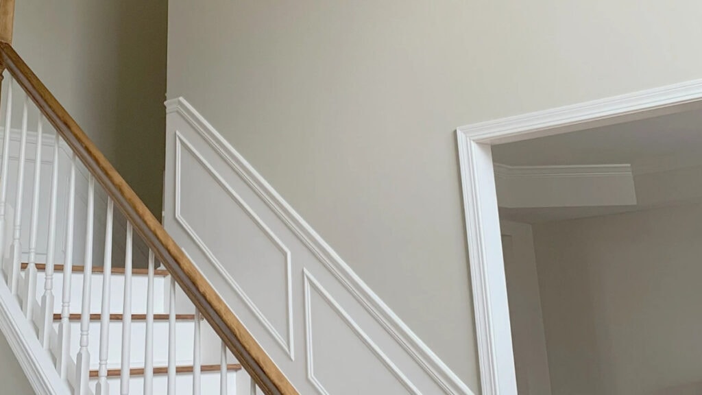 Benjamin Moore Grant Beige in staircase with Cloud White wainscoting and wood hand railing