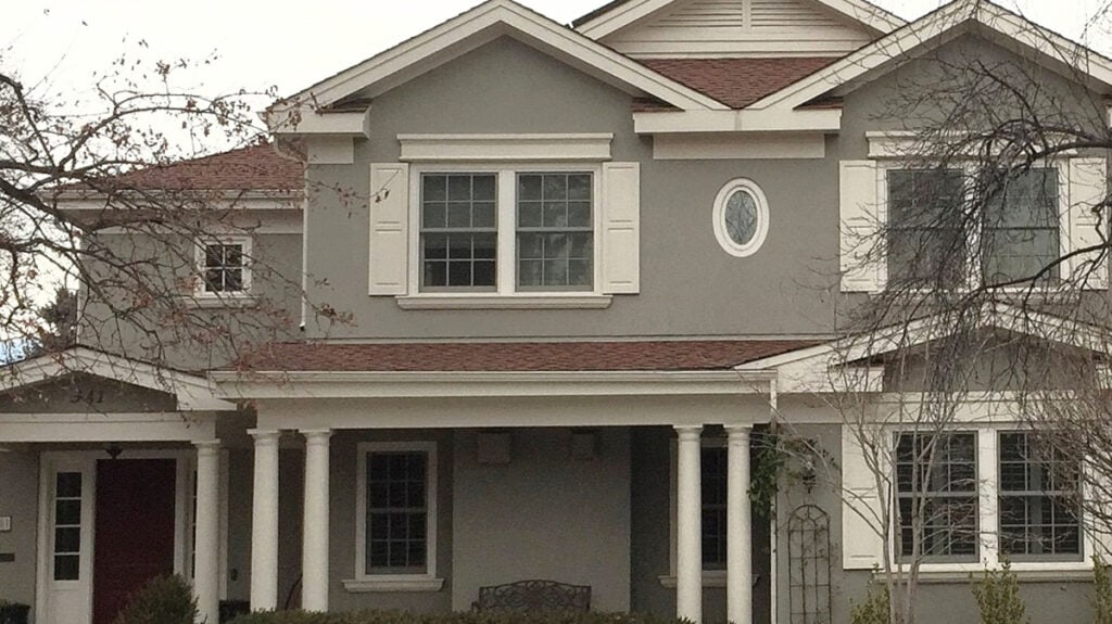 Benjamin Moore Rockport Gray painted stucco exterior with Sail Cloth trim and shutters and orange-red asphalt roof in shade