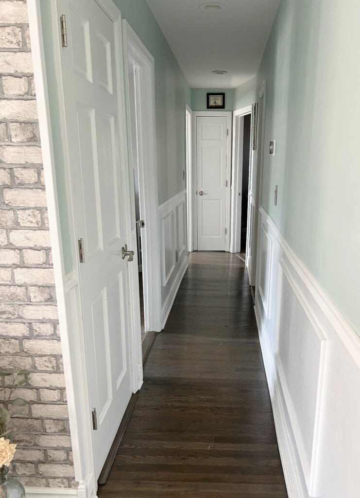 Benjamin Moore Palladian Blue, blue green walls with dark wood floor, white wainscoting, pink violet gray toned brick accent. best paint color dark hallway