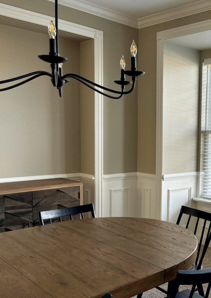 Warm neutral beige-tan, Sherwi Williams Tony Taupe, in dining room with white wainscoting, oval wood table, black chairs, crown molding
