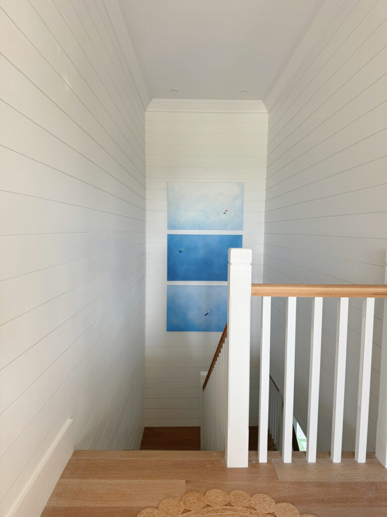 Staircase and landing with beach artwork, wood floor, railing, Sherwin Williams Snowbound shiplap walls