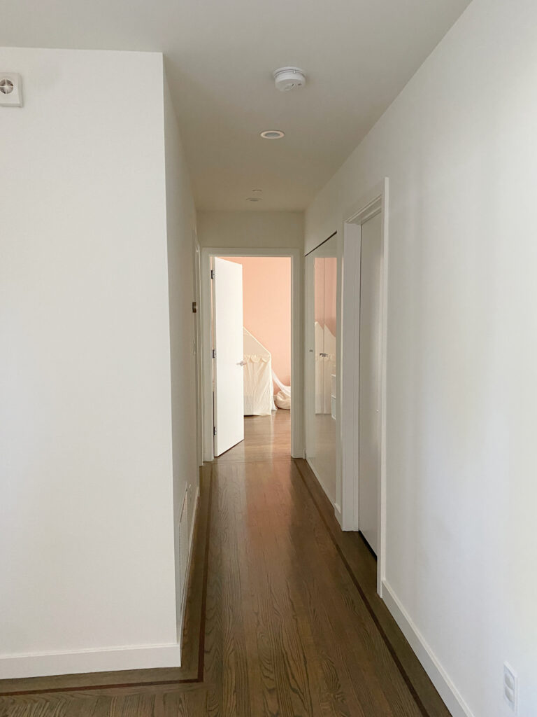 dark hallway painted Kelly Moore Swiss Coffee, dark wood floor, pink bedroom at the end. Similar to Benjamin Moore White Dove (LRV 83.16)