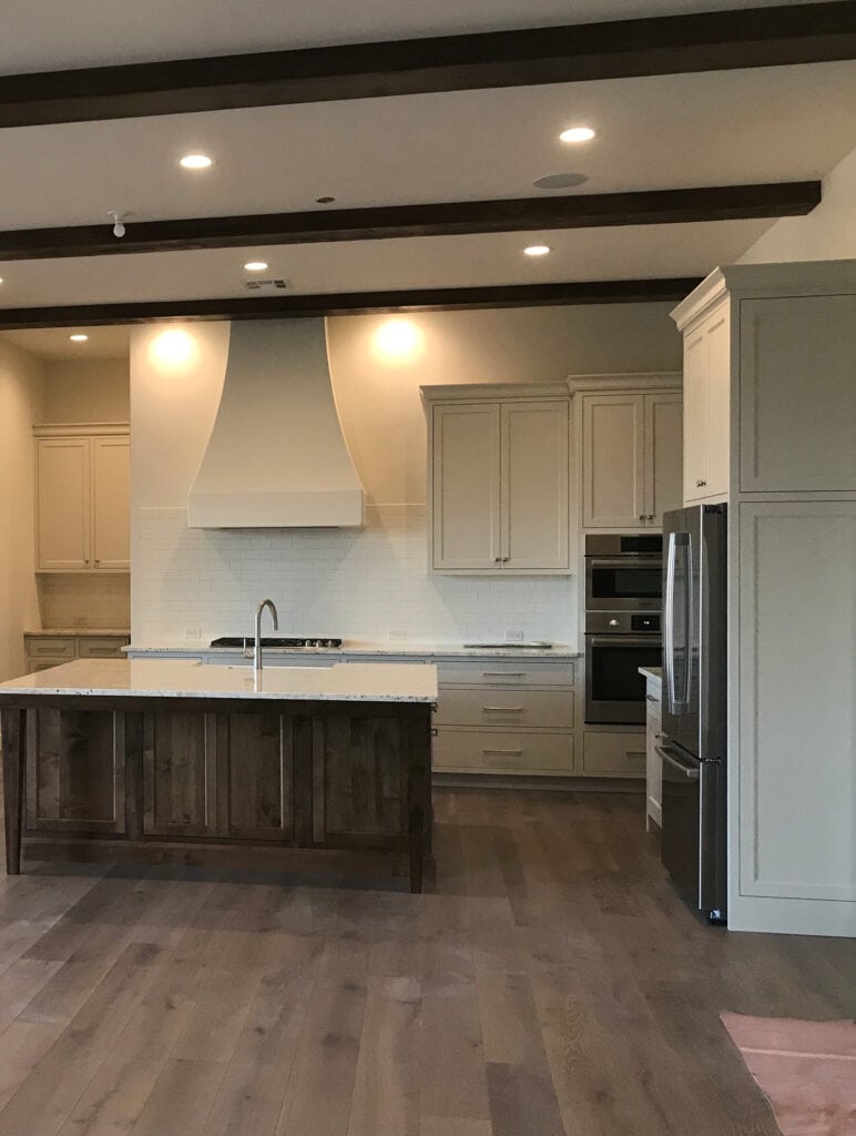 Benjamin Moore Edgecomb Gray paint color on kitchen cabinets, dark wood stained island, wood floor, off-white quartz countertop, range hood, off white walls