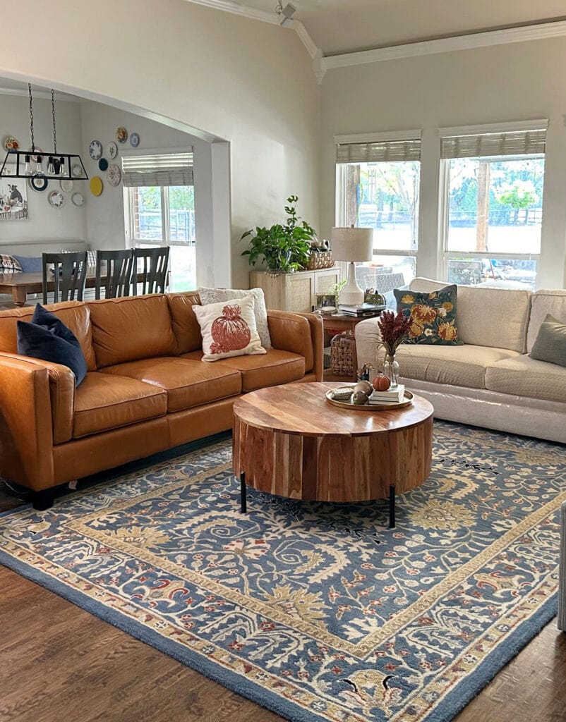 Cognac leather sofa in living room, beige sofa, blue area rug, round coffee table, Benjamin Moore Winds Breath off-white paint color on walls