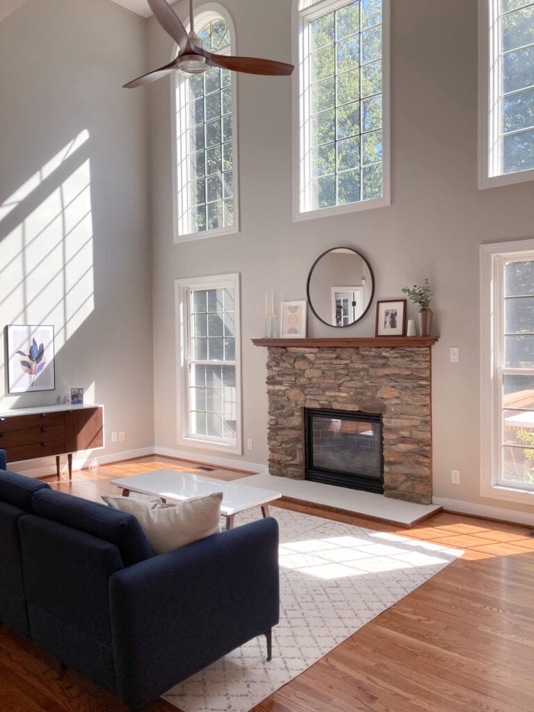 Living room with tall ceilings, brown stone fireplace, Benjamin Moore Edgecomb Gray greige, taupe paint color on walls, orange hue oak floor. Kylie M Interiors Edesign, client photo