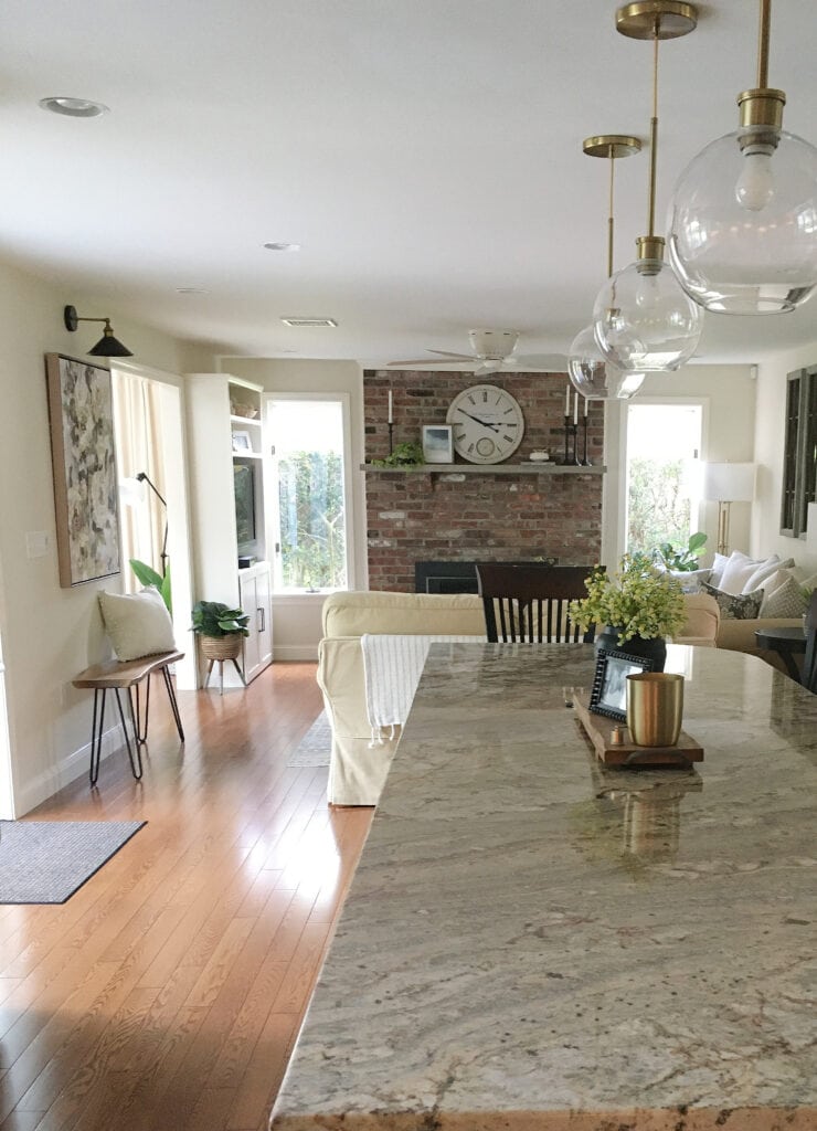Older style granite countertop on kitchen island, red oak flooring, brick fireplace, Sherwin Williams Neutral Ground paint color on walls, glass round pendant lights