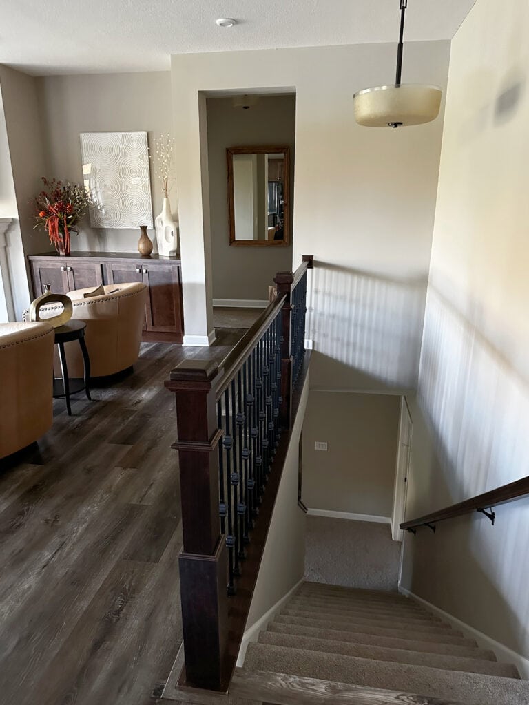 Sherwin Williams Amazing Gray, staircase with carpet, laminate or LVP wood look floor, PUre White trim, dark wood railing with black spindles.
