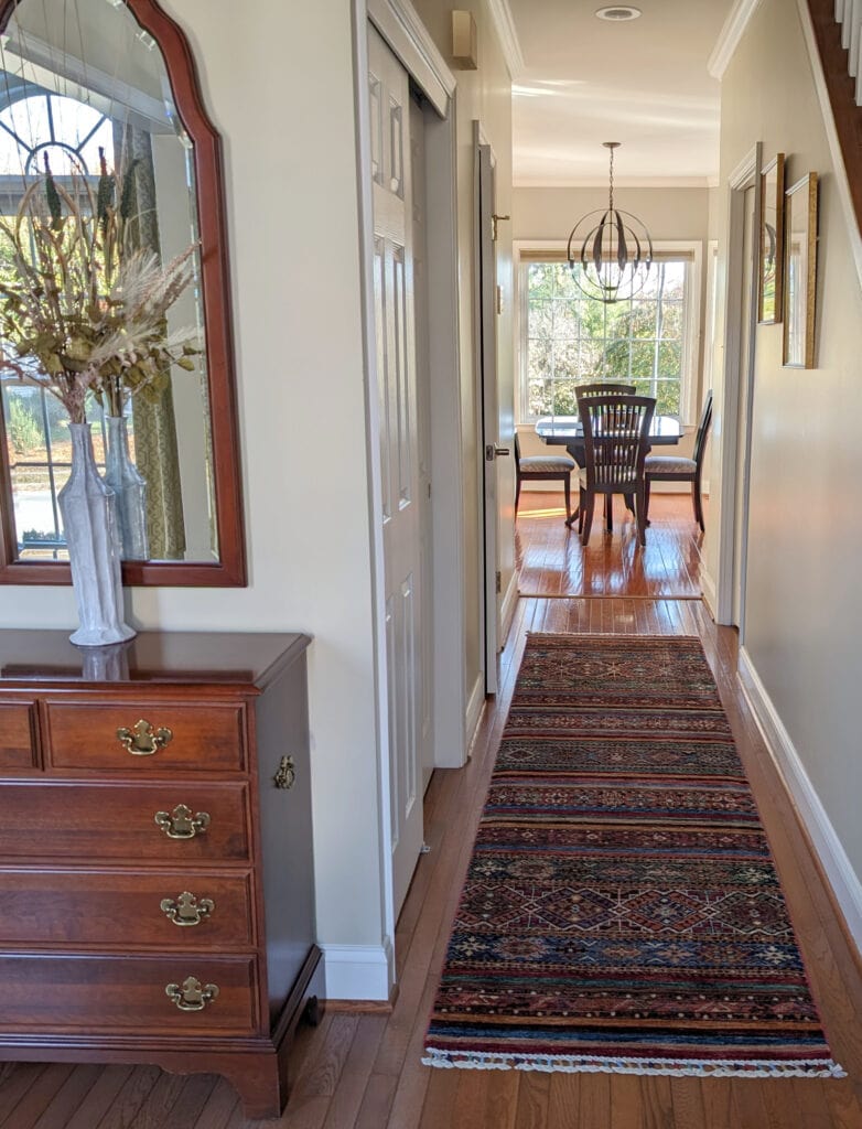 Sherwin Williams Dirty Martini in entryway and hallway, dark red wood stain cherry furniture and oak floor, colorful runner, white trim, strong tan paint color