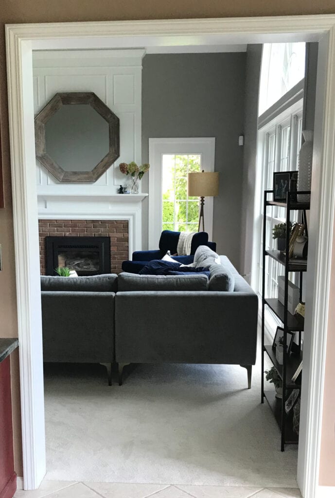 Sherwin Williams Dovetail in living or family room, fireplace vaulted with white moldings, mirror, brick surround, gray sectional and beige neutral carpet