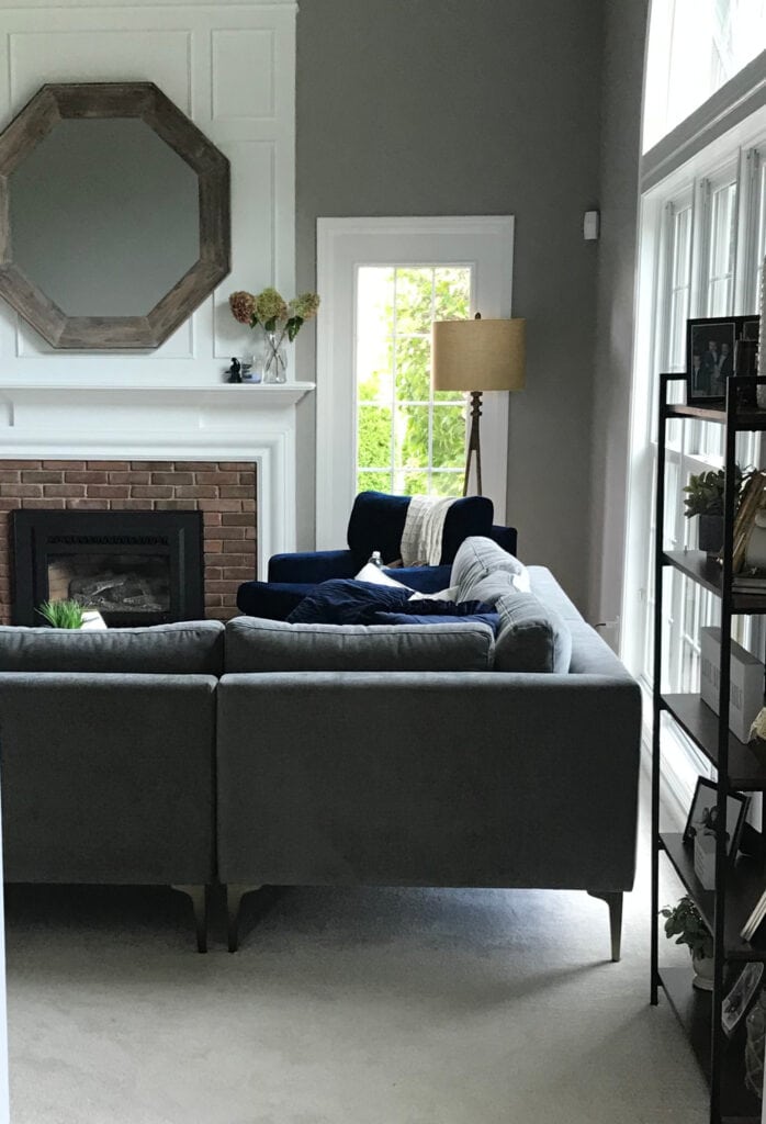 Sherwin Williams Dovetail in living room, fireplace vaulted with white moldings, mirror, brick surround, gray sectional and beige neutral carpet