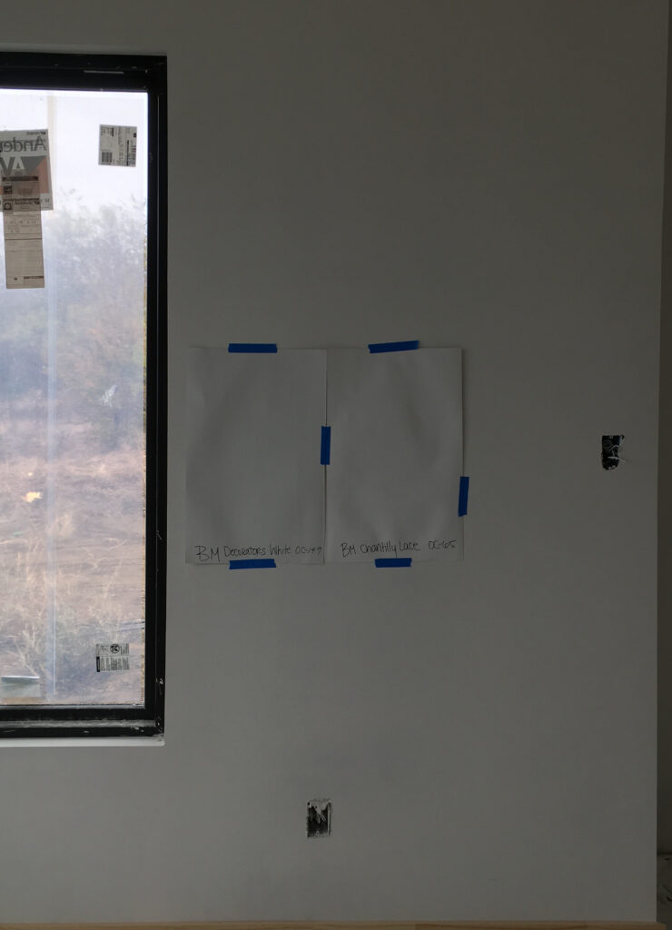 Benjamin Moore Decorators White vs Chantilly Lace paint samples on wall with no natural light or a dark room