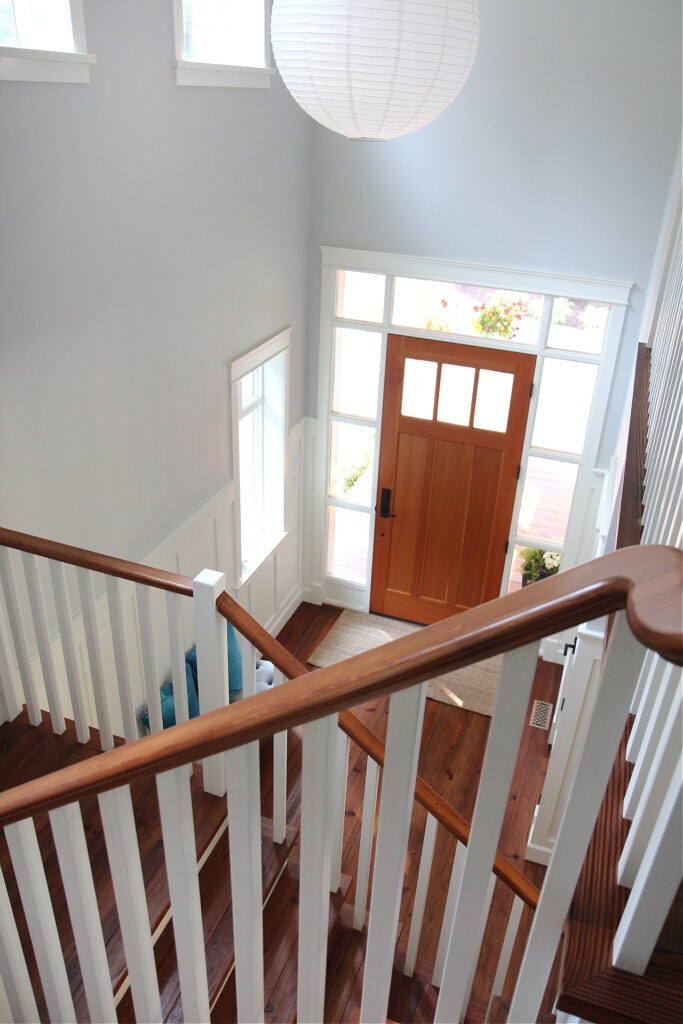 Benjamin Moore Gray Owl in two storey entryway, wood staircase railing with white spindles, fir front door, Cloud White wainscoting and trim
