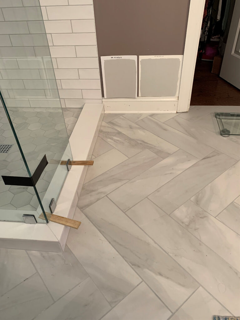 Benjamin Moore NIMBUS AND Sherwin Williams ON THE ROCKS with herringbone tile, marble-look floor in bathroom with white subway tile wall