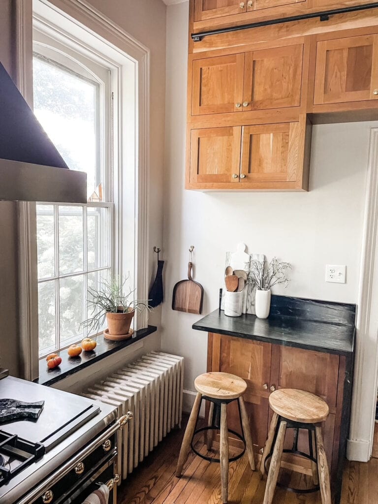 Cherry stained wood kitchen cabinets, heritage home, oak floor, black soapstone countertop and backsplash, radiator. Benjamin Moore Pale Oak paint color walls