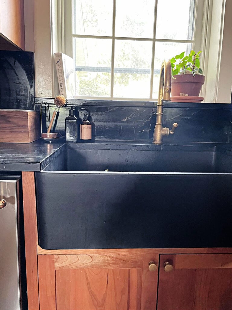 Cherry wood stained kitchen cabinets, black farmhouse style sink, soapstonen countertop and backsplash, gold faucet
