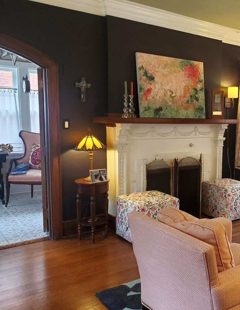 Heritage home with oak wood floor, white fireplace surround, Sherwin Williams Black Swan, dark purple paint color, green ceiling, pink and green accents, dark wood trim in arched doorway