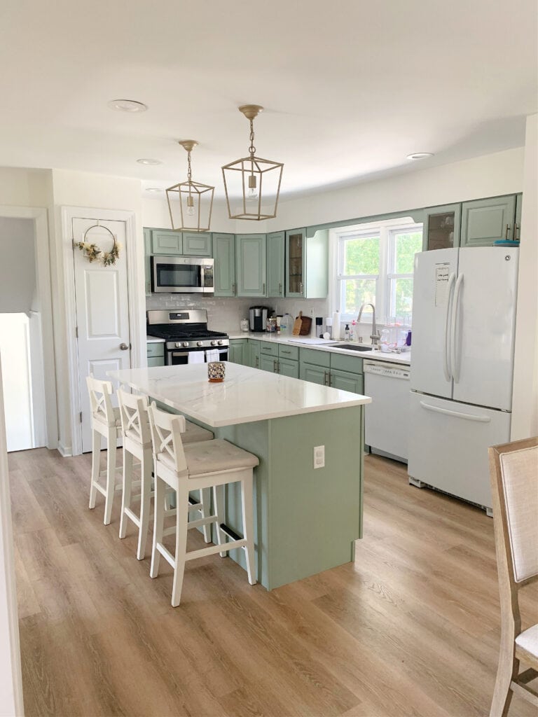 Sage Green painted kitchen cabinets, benjamin Moore Cascade Green, wood look floor, white appliances, white quartz updated countertop and subway tile nbacksplash, gold hardware, island