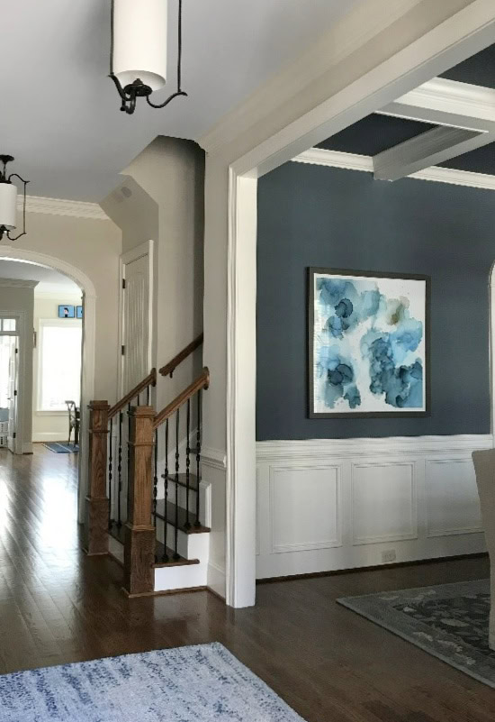 Sherwin Williams Wall Street in dining room with coffered ceiling and white wainscoting, hallway entryway in Sherwin Williams Wool Skein with dark wood floor and gray-blue ceiling paint color