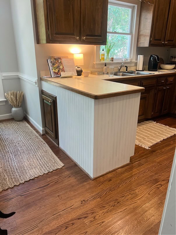 before update, kitchen with beadboard peninsula, off-white laminate countertop, oak floor, dark wood stained cabinets