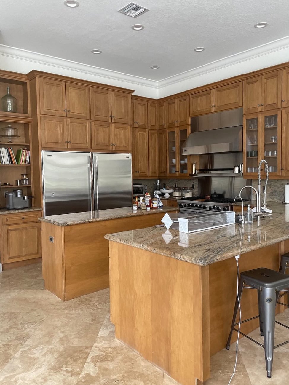 before update, kitchen with stained maple or cherry wood cabinets, granite countertop, travertine look tile floor, stainless steel appliances and double fridge.