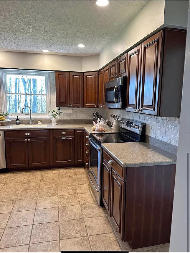 dark red stained wood kitchen cabinets, beige and brown tile floor, painted backsplash, corian gray taupe countertop,