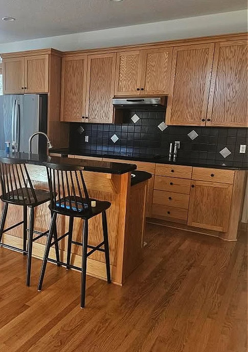 golden oak kitchen cabinets, timeless style with oak floor, black corian or granite countertop on raised island, black tile backsplash, wood trim