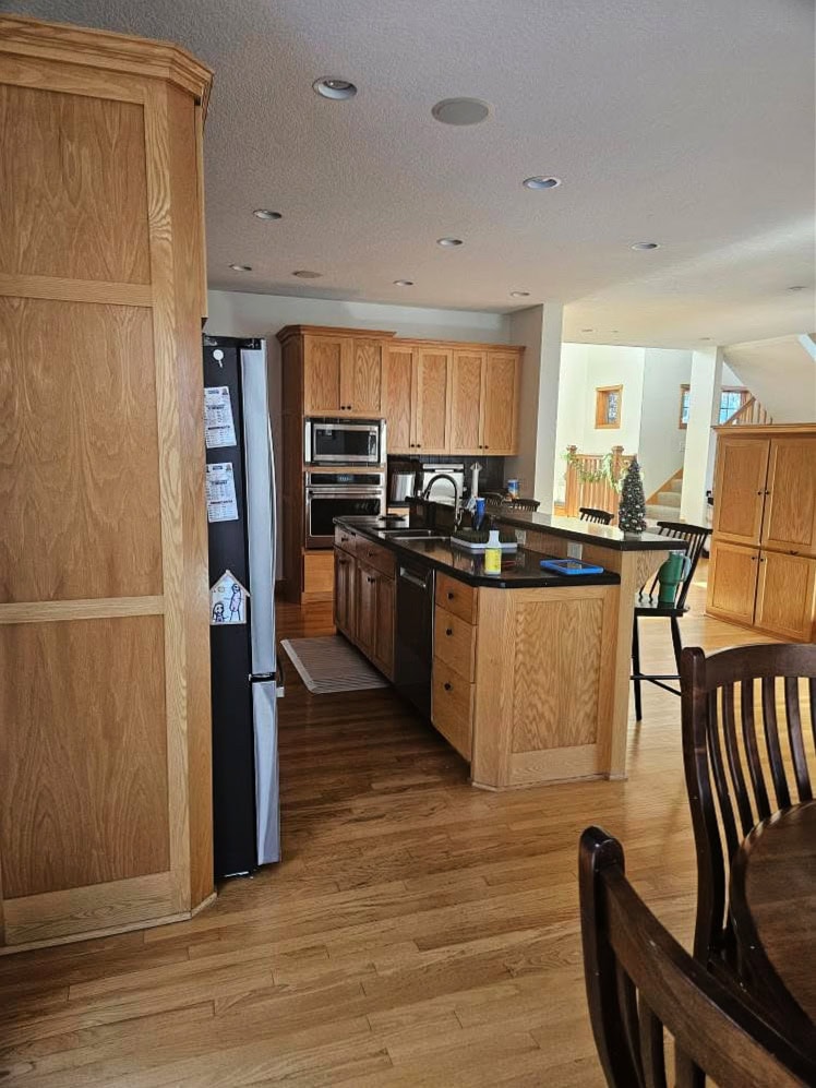 kitchen with golden oak wood cabinets and flooring, black raised island countertop with bar area,