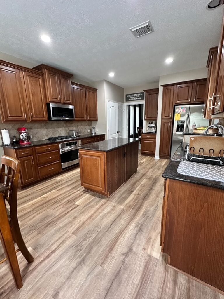 kitchen with wood look floor, dark red cherry or maple stained cabinets with island, dark black granite countertops, tile backsplash, small island