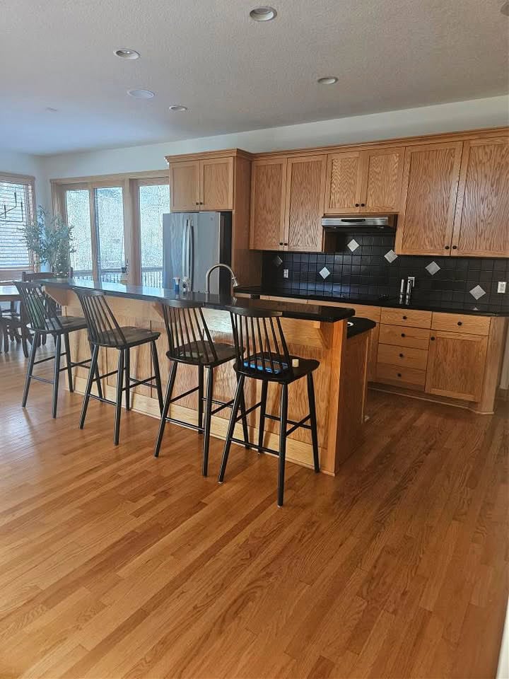 wood trim, golden oak wood cabinets and floor, raised kitchen island with black granite or corian countertops, stainless steel appliances