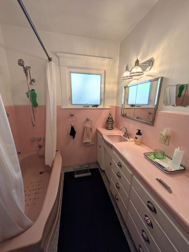 1960 bathroom with pink tiled wall, countertop, pink fixtures and bathtub, white paint color on walls